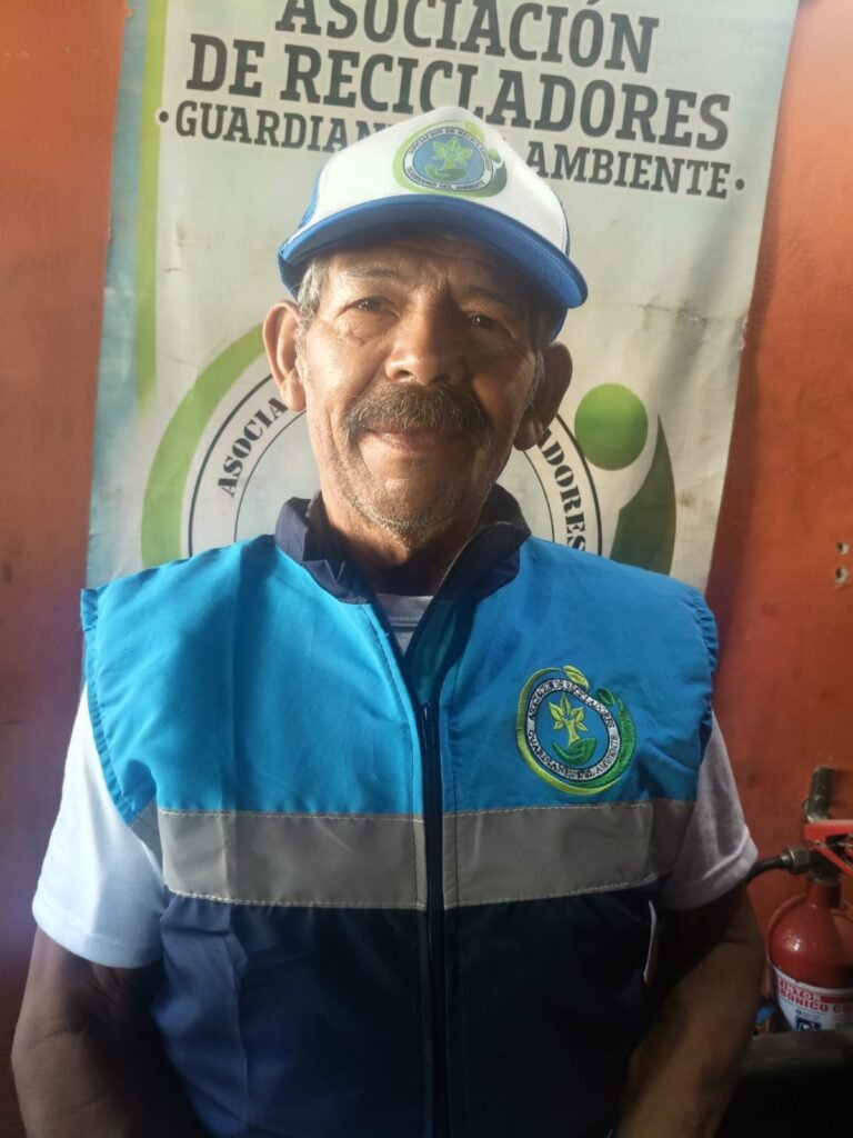 Reciclador asociado a Guardianes del Ambiente con chaleco y gorra institucional, frente al pendón de la asociación en Villavicencio