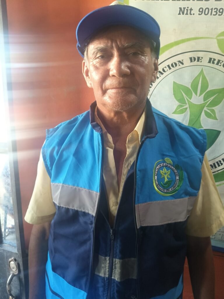 Asociado reciclador con chaleco reflectivo y gorra de Guardianes del Ambiente frente al logo de la asociación