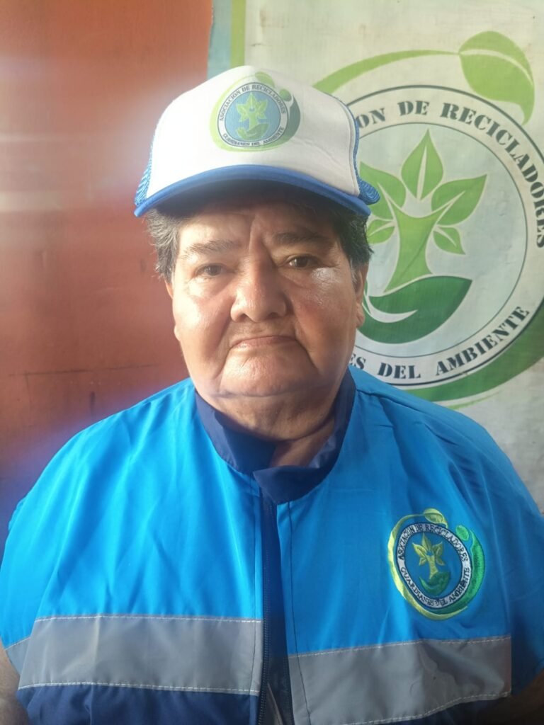 Asociado de Guardianes del Ambiente con chaleco institucional frente al pendón de la Asociación de Recicladores